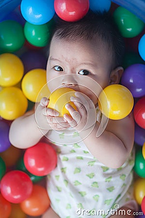 Cute baby lying in colorful toy balls and playing happily Stock Photo