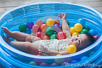 Cute baby lying in colorful toy balls and playing happily Stock Photo