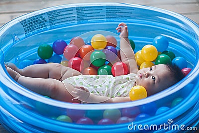 Cute baby lying in colorful toy balls and playing happily Stock Photo