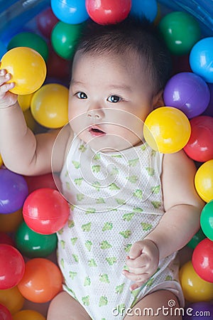 Cute baby lying in colorful toy balls and playing happily Stock Photo