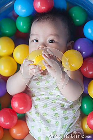 Cute baby lying in colorful toy balls and playing happily Stock Photo