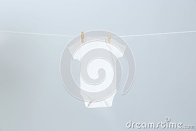 Cute baby onesie hanging on clothes line against light grey background Stock Photo