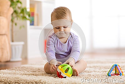 Cute baby playing with colorful toys sitting on carpet in white sunny bedroom. Child with educational toy. Early Stock Photo