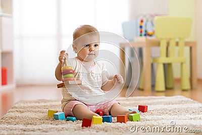 Cute baby playing with colorful toys sitting on carpet in white sunny bedroom. Child with educational toys. Early Stock Photo