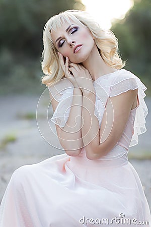 Cute beautiful girl blonde curly hair walking in the woods in a wedding dress in the sun at sunset Stock Photo