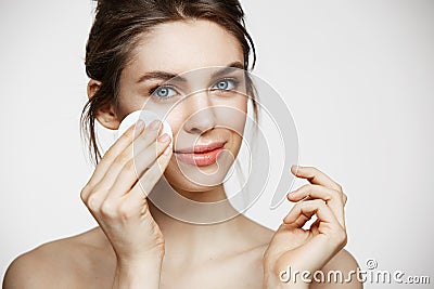 Cute beautiful natural brunette girl cleaning face with cotton sponge smiling looking at camera over white background Stock Photo