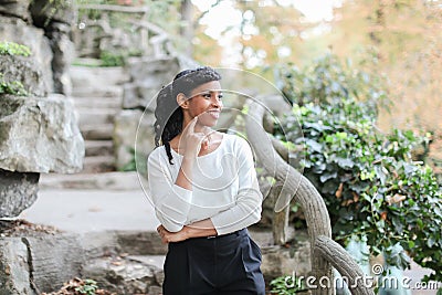 Cute black female person standing near rock and stone stairs in park, having ponytail. Stock Photo