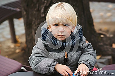 Cute blond baby boy playing with toys outdoors. Toddler boy with blue eyes and blonde hair. Child in warm jacket at walk in cold Stock Photo