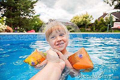 A cute blond baby girl at swimming pool with blue colored water , hold parent`s hand and fells happy. Stock Photo