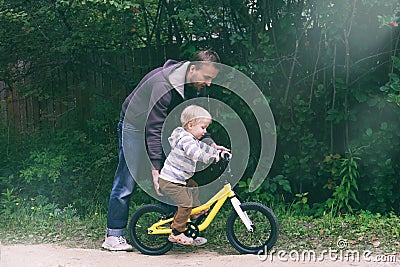 Cute blond boy learning to ride bicycle. Father teaching his little child to ride bike in spring summer park. Happy family moments Stock Photo