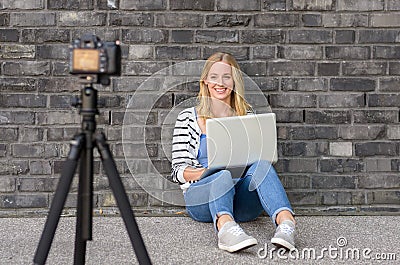 Cute blond female blogger with laptop recording video Stock Photo