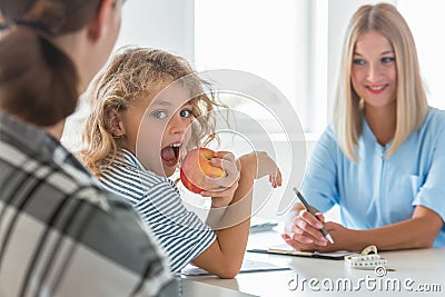 Blond haired boy eating an apple while visiting a dietitian Stock Photo