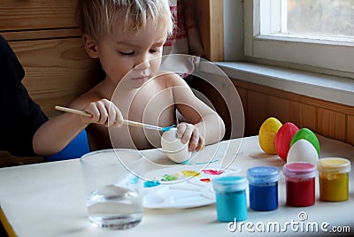 Cute blond boy dyeing Easter eggs at home. Candid photo with natural light Stock Photo