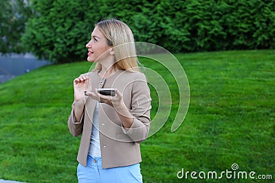 Cute blonde holds phone in hands, looks around and smiles enigma Stock Photo