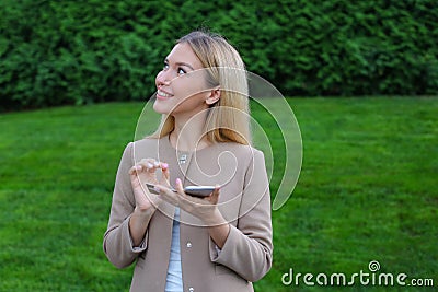 Cute blonde holds phone in hands, looks around and smiles enigma Stock Photo