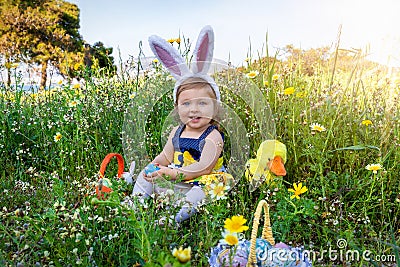 A cute, blue eyed baby girl on a easter egg hunt ourdoors in the meadow Stock Photo