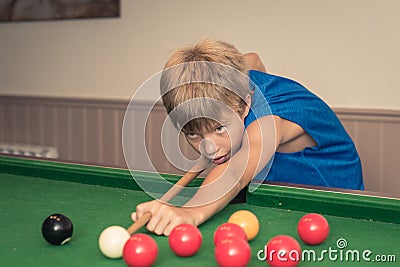 Cute boy in blue t shirt plays billiard or pool in club. Young Kid learns to play snooker. Stock Photo