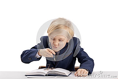 Cute boy first grader in school uniform fooling around while sitting at his desk. Schoolboy plays and makes face while doing Stock Photo
