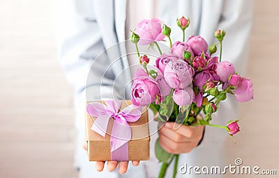 Cute boy holding gift box and bouquet flowers for mother a with falling petals. Greeting card for Mother`s Day Stock Photo