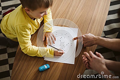 Cute boy kneeling on the floor and connecting dots on a piece of paper Stock Photo