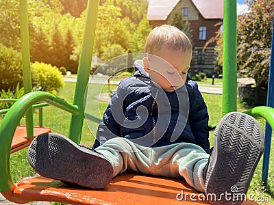 A cute boy of one and a half years rides on a swing. Backyard of the house. Childrens entertainment. Selective focus Stock Photo