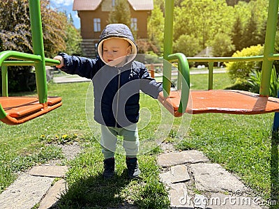 A cute boy of one and a half years standing near the swing. Backyard of the house. Children`s entertainment. Selective focus Stock Photo