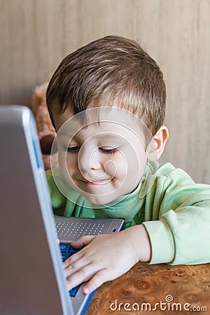 Cute boy is pushing laptops keyboard and he is looking at the screen. Stock Photo