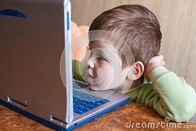 Cute boy is pushing laptops keyboard and he is looking at the screen. Stock Photo