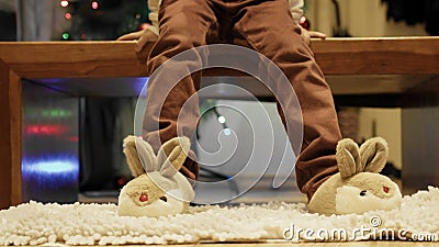 Cute boy sitting near the Christmas tree and playing with his new bunny slippers. Stock Photo