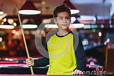 Cute boy in yellow t shirt plays billiard or pool in club. Young Kid learns to play snooker. Boy with billiard cue Stock Photo