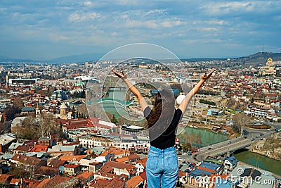 A cute brunette girl enjoys the stunning scenery of Tbilisi from the hill. The whole city at her feet Stock Photo