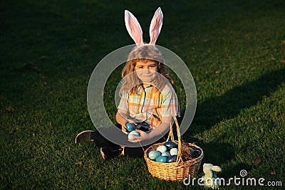 Cute bunny child with rabbit ears. Child boy hunting easter eggs in spring lawn laying on grass. Stock Photo