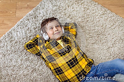 Cute carefree little boy resting on floor at home, listening to music via headphones and dreaming, top view, free space Stock Photo