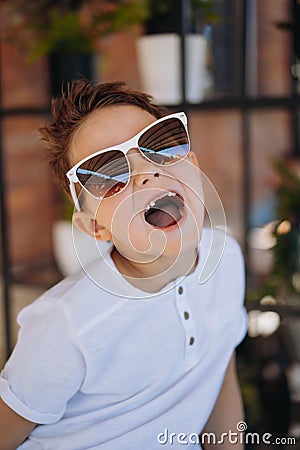 Cute cauasian boy in white tee shirt and sunglasses posing for camera and showing his lost tooth. Stock Photo