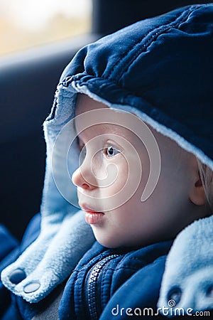 Cute Caucasian baby infant sitting in car seat. Adorable kid in outwear clothes in automobile vehicle carsit fastened with Stock Photo