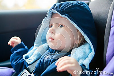 Cute Caucasian baby infant sitting in car seat. Adorable kid in outwear clothes in automobile vehicle carsit fastened with Stock Photo