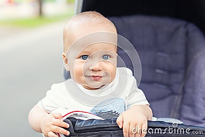 Cute caucasian blond curious baby boy sitting in stroller , smiling, looking and aspiring to something outdoor at city park. Stock Photo