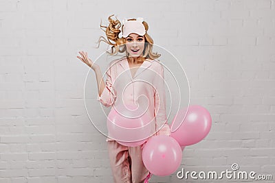 Cute caucasian lady in sleepmask jumping on white background with party balloons. Studio shot of amazed attractive Stock Photo