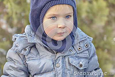 Cute caucasian liittle boy with big bright blue eyes in winter clothes and hat hood on green background. Healthy childhood. Stock Photo