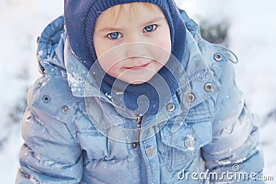 Cute caucasian liittle boy with bright blue eyes in winter clothes and hat hood on winter background. Healthy childhood. Outdoor Stock Photo