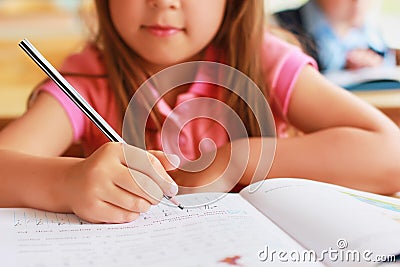 A sweet Caucasian child in school at a desk writes in a notebook Stock Photo