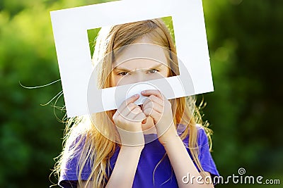 Cute cheerful little girl holding white picture frame in front of her face Stock Photo