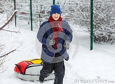 Cute, cheerful young boy in hat, blue jacket plays with snow, has fun, smiles, makes snowman in winter park. Stock Photo