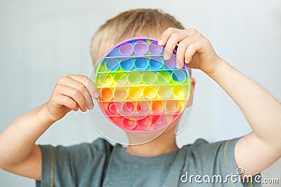 Cute child boy playing with antistress pop it fidget toy. Kid holding trendy silicone pressure relieving sensory board game simple Stock Photo