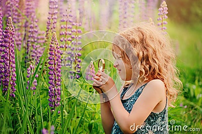 Cute child girl exploring nature with loupe on summer field Stock Photo