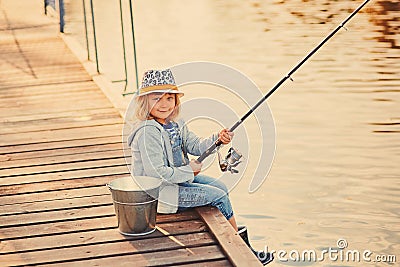 Cute child girl fishing from wooden pier on a lake. Family leisure activity during summer sunny day. little girl having fun by a Stock Photo