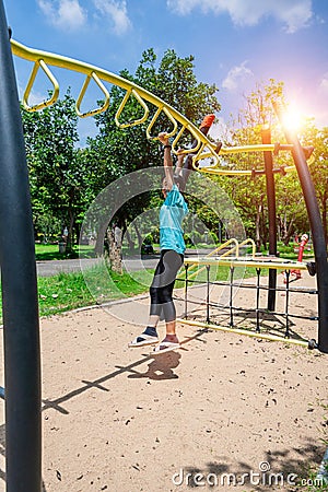 Cute child girl hanging hanging on monkey bars at the playground in park outdoor. Cute little girl having fun on summer garden Stock Photo