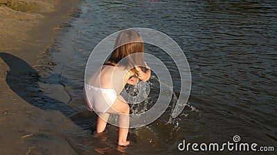 Cute child happily plays on the beach. baby splashing in the water. splashing water. happy child bathes in the sunset on Stock Photo