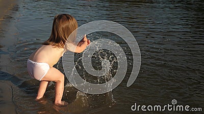 Cute child happily plays on the beach. baby splashing in the water. splashing water. happy child bathes in the sunset on Stock Photo