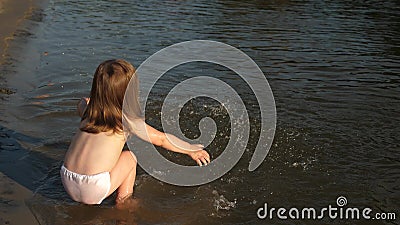 Cute child happily plays on the beach. baby splashing in the water. splashing water. happy child bathes in the sunset on Stock Photo